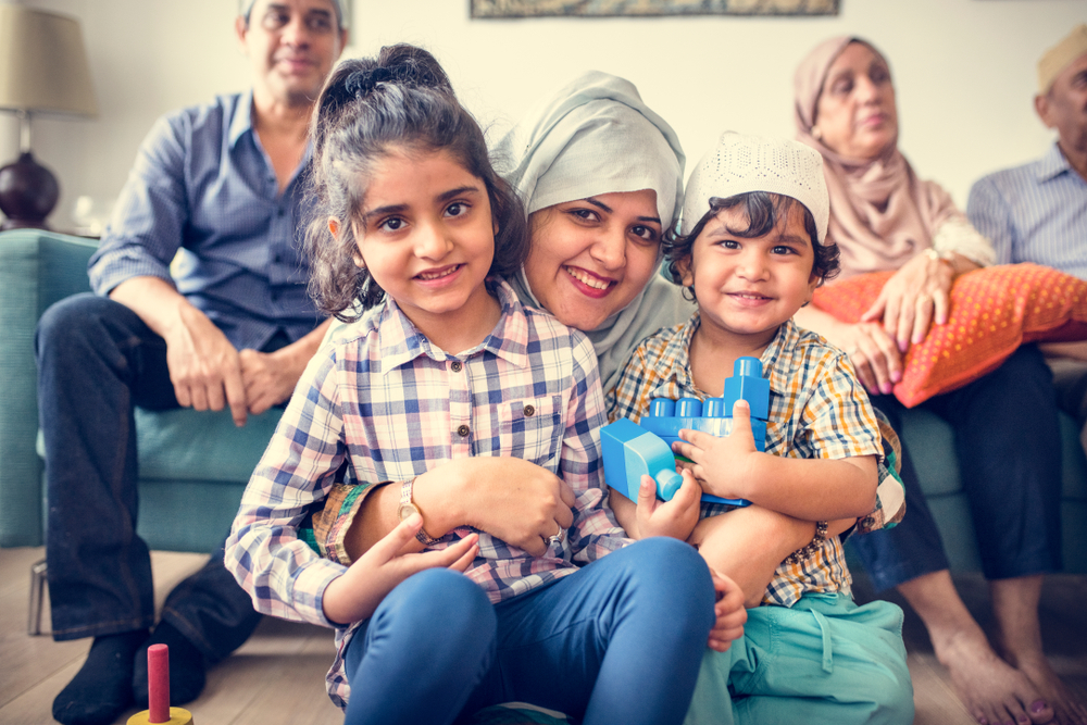 A Muslim family sitting on and around the sofa in their living room loading=