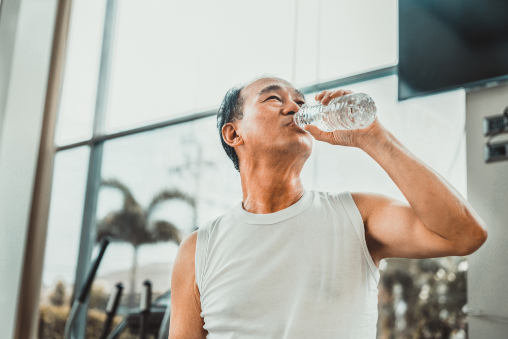 An older asian man in the gym, drinking water to rehydrate loading=