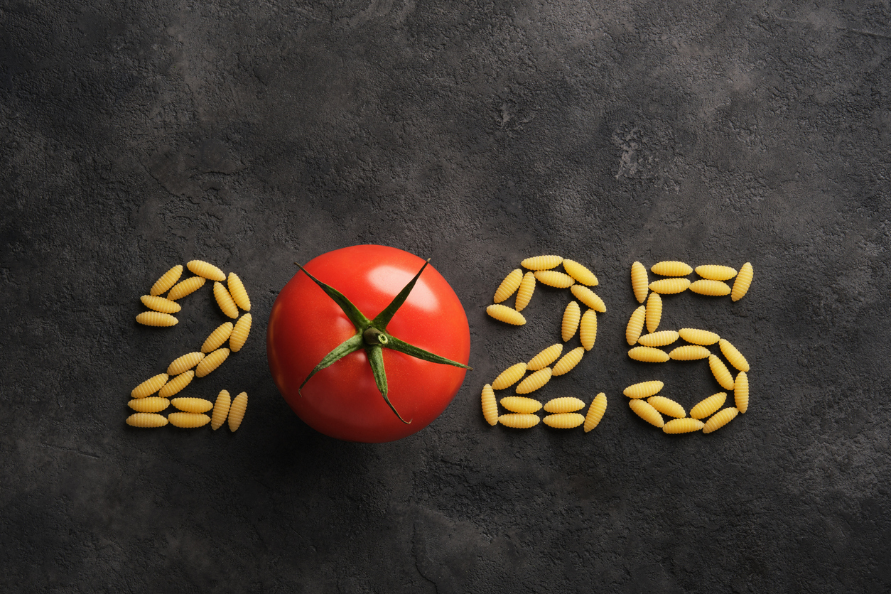 A chalkboard background with the word '2025' written on it. The letters are formed from pasta, except the zero, which is replaced by a tomato loading=